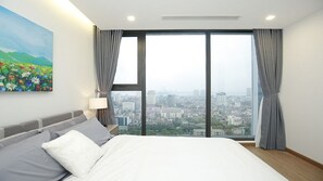 A modern hotel room with a large bed, a city view, and a painting on the wall.