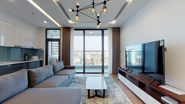 Una sala de estar moderna con un sofá, una mesa de centro, un televisor y vistas de la ciudad a través de grandes ventanales.