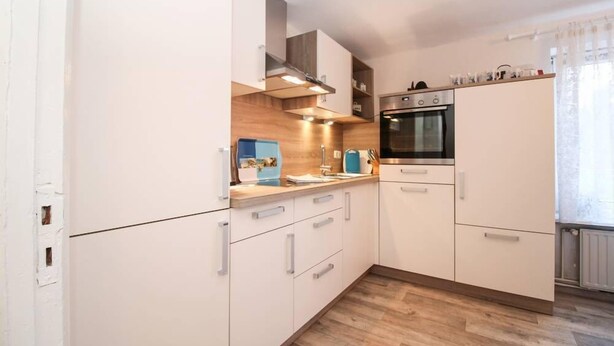 A modern kitchen with white cabinets, a built-in oven, and a wooden countertop.