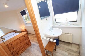 A bedroom with a wooden bed, a small bedside table, a window with a view, a white sink, and a radiator.