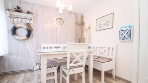 A dining area with a white table and chairs, a clock on the wall, and nautical-themed decor.