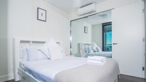 Une chambre d’hôtel moderne équipée d’un lit, d’une table de chevet, d’un miroir et d’un appareil de climatisation.