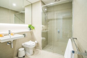 A modern bathroom with a glass-enclosed shower, a white sink with a mirror above it, and a toilet.