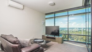 Un salon moderne avec un canapé en cuir, un téléviseur à écran plat et une grande fenêtre donnant sur la ville.