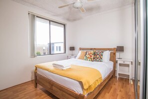 A bedroom with a wooden bed, a yellow throw blanket, two bedside tables with lamps, and a window with curtains. - Simple Comfort! 2bed1bath Unit in Meadowbank (Meadowbank)