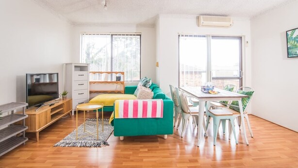 A bright living room with a green sofa, a TV, and a dining area with a table and chairs. - Simple Comfort! 2bed1bath Unit in Meadowbank (Meadowbank)