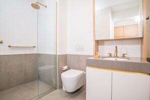 Um banheiro moderno com chuveiro de vidro, vaso sanitário e pia com bancada.