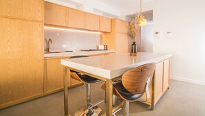 A modern kitchen with wooden cabinets, a white countertop, and two bar stools. - Inner City Penthouse With Private Rooftop (Waterloo)