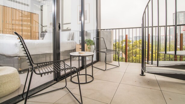 A modern hotel room with a balcony, a bed, a small table, and two chairs. - Inner City Penthouse With Private Rooftop (Waterloo)