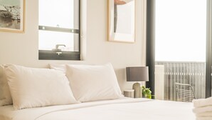A hotel room with a large bed, a bedside table with a lamp, a window with a view of a building, and a framed picture on the wall. - Inner City Penthouse With Private Rooftop (Waterloo)