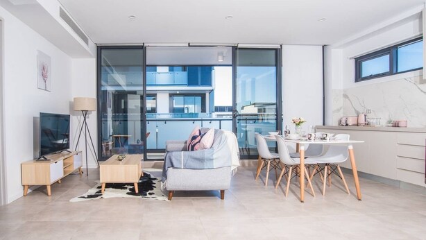 Una sala de estar moderna con sofá, televisor y comedor con sillas y mesa.