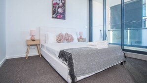 Un dormitorio moderno con una cama grande, dos mesitas de noche con lámparas, una obra de arte en la pared y vistas a través de un ventanal amplio.