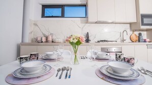Una cocina moderna con encimeras de mármol, una mesa de comedor dispuesta con platos, tazones y cubiertos blancos, y un florero con flores.