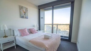 Ein Schlafzimmer mit einem großen Fenster, einem Bett mit pinkener Bettwäsche, einem Nachttisch mit Lampe und einem Bild an der Wand.