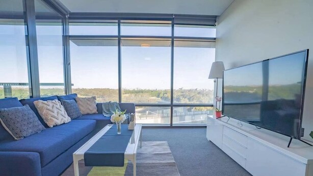 Ein modernes Wohnzimmer mit einem großen Fenster, einem blauen Sofa, einem Couchtisch und einem Flachbildfernseher.