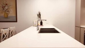 Eine moderne Küche mit weißer Arbeitsplatte, integriertem Spülbecken und einer kleinen Kochinsel.