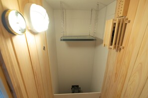 A small, enclosed room with a hanging shelf, a clock, and a wooden cabinet.