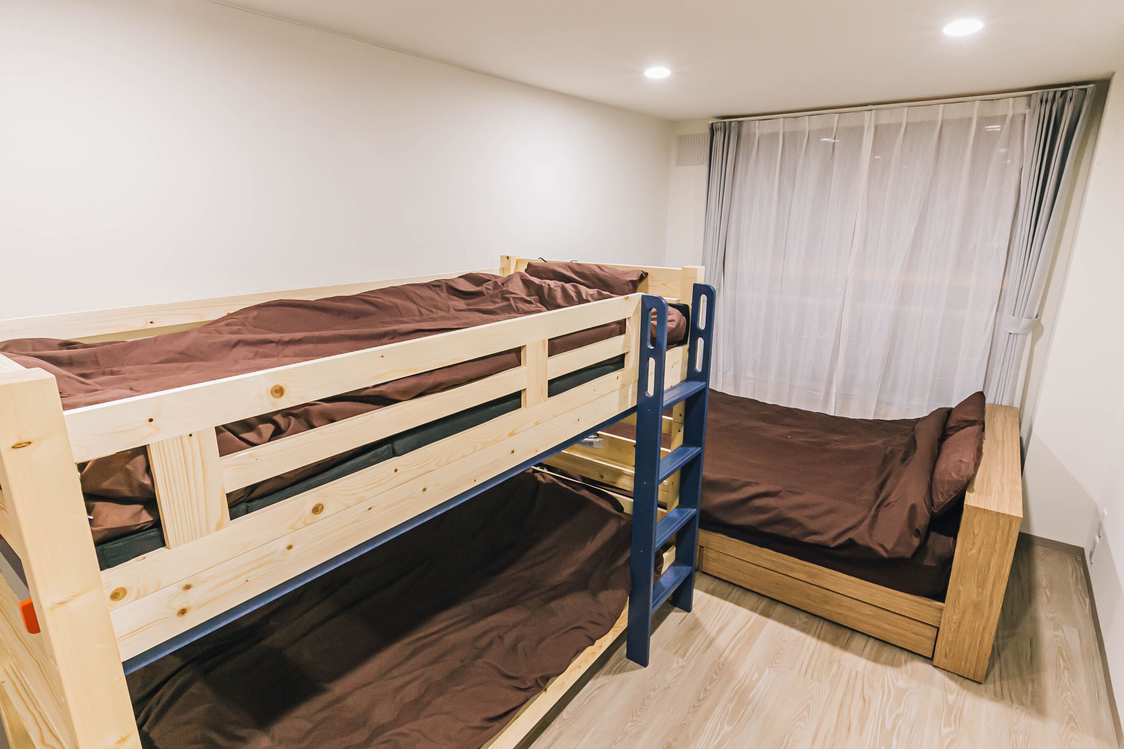 A bunk bed room with a wooden frame, a lower bunk with a mattress, and a single bed with a mattress.