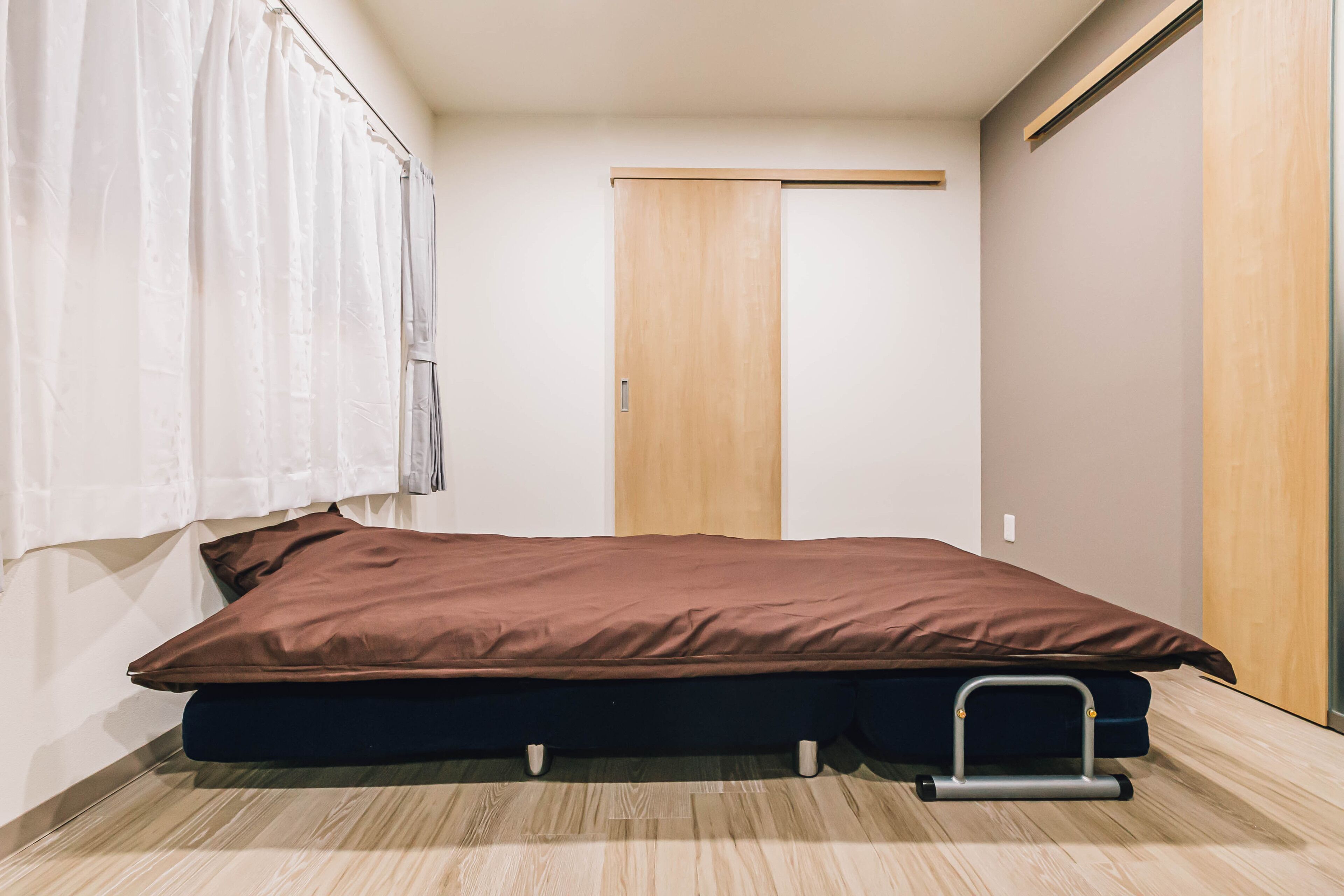 Une petite chambre avec un lit simple, une armoire en bois, une fenêtre avec des rideaux et un plancher de couleur claire.