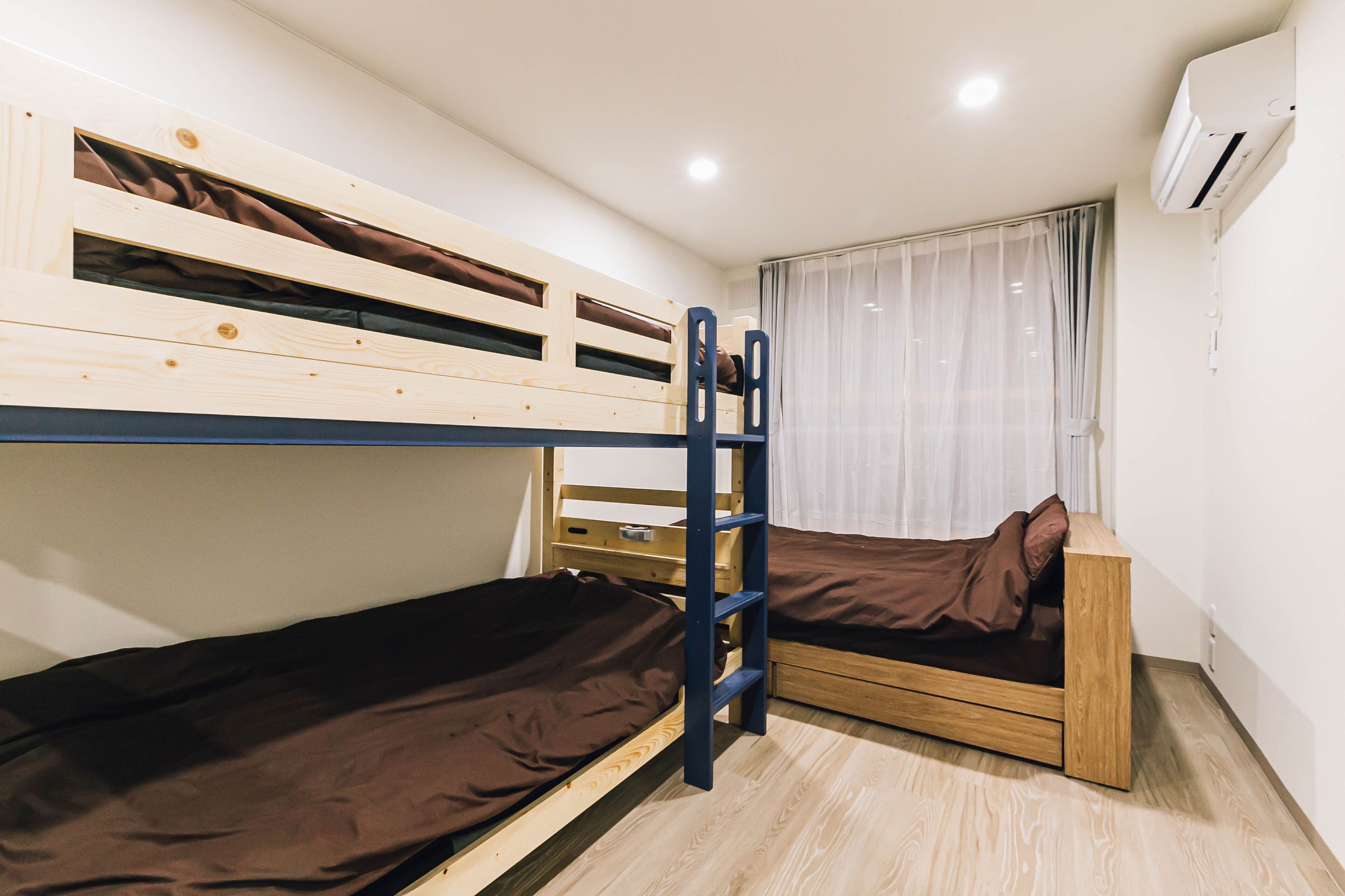 A bunk bed room with a ladder, a window with curtains, and an air conditioning unit.