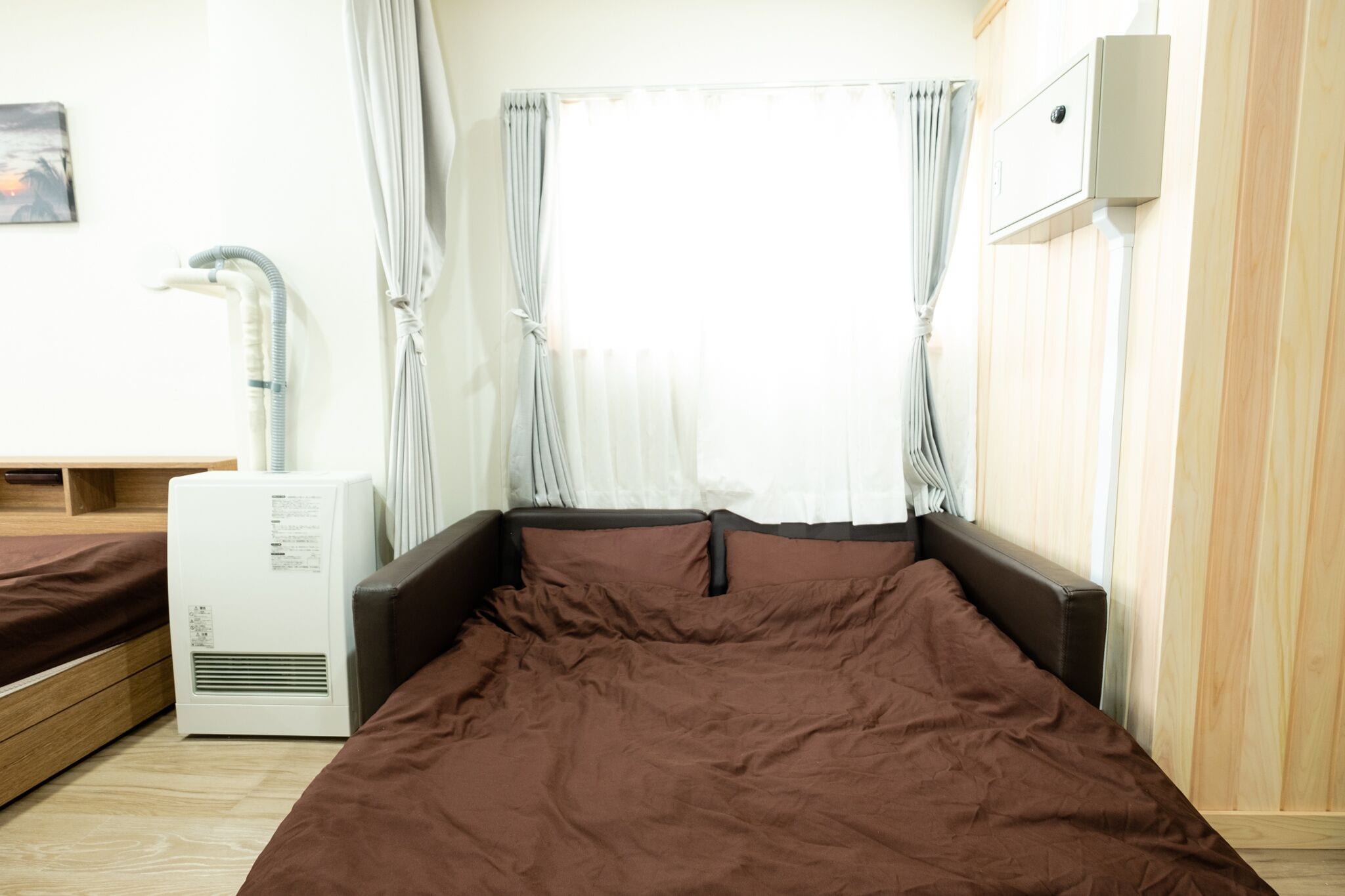 A bedroom with a bed, a heater, and a window with curtains.