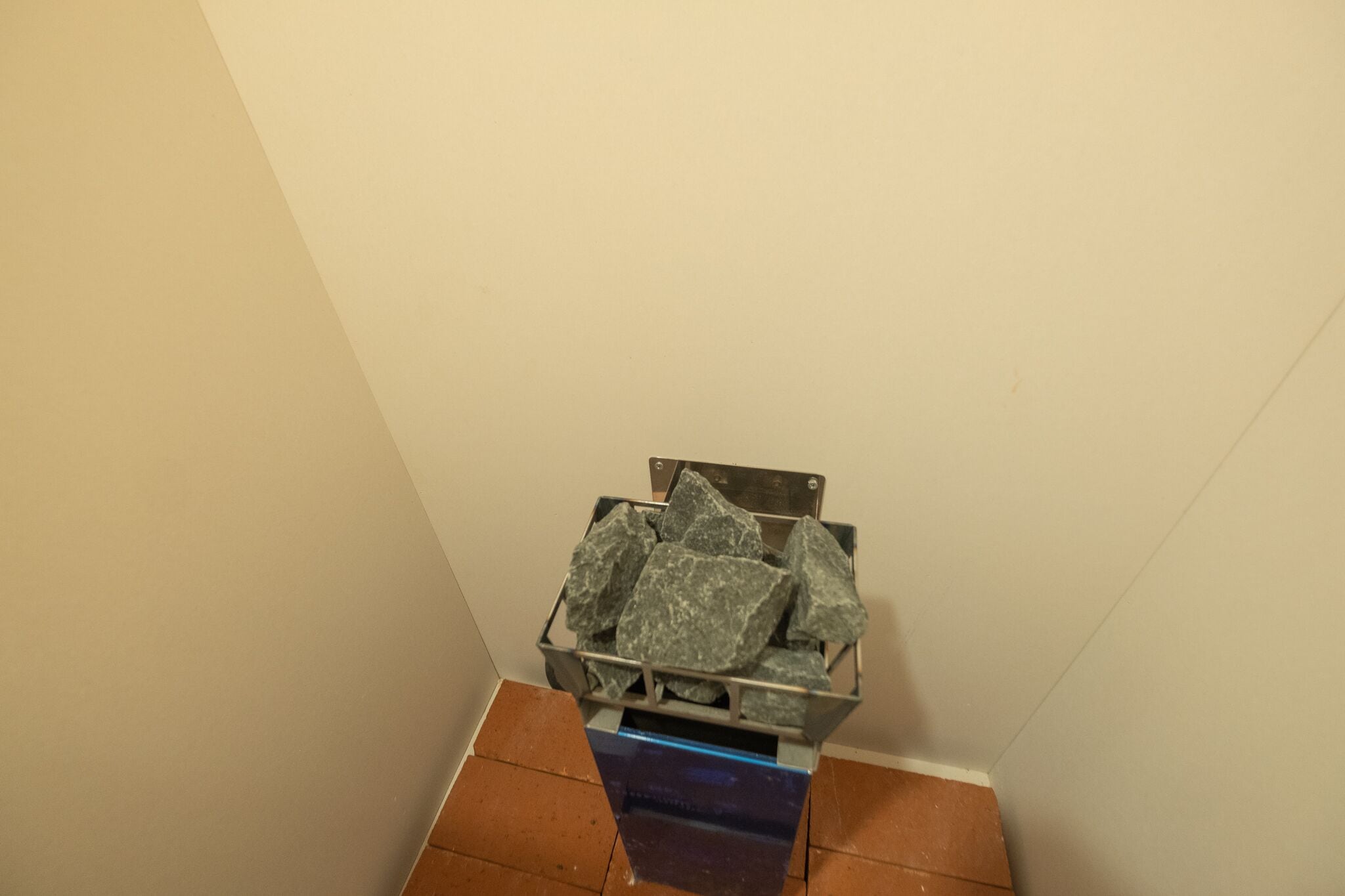 A corner of a room with a metal bin filled with rocks on a tiled floor.