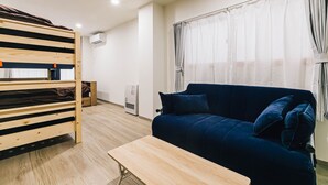 Une pièce avec un lit superposé, un canapé bleu, une table en bois et une fenêtre avec des rideaux.