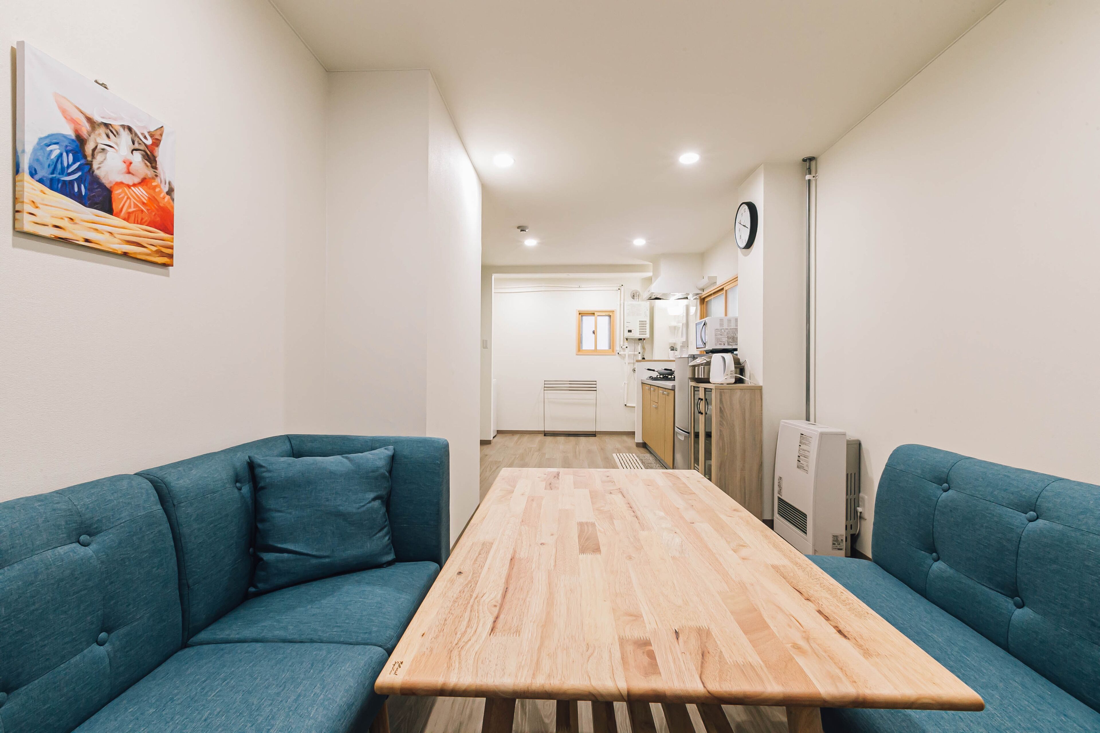 Un salon moderne avec une table en bois et deux canapés bleus. On aperçoit une cuisine à l’arrière-plan, avec un réfrigérateur et un four à micro-ondes.