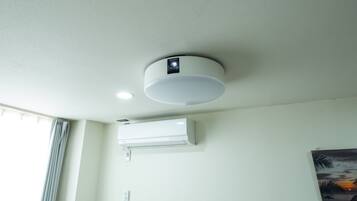 A ceiling-mounted air conditioning unit and a smoke detector in a room with a window and a wall-mounted painting.