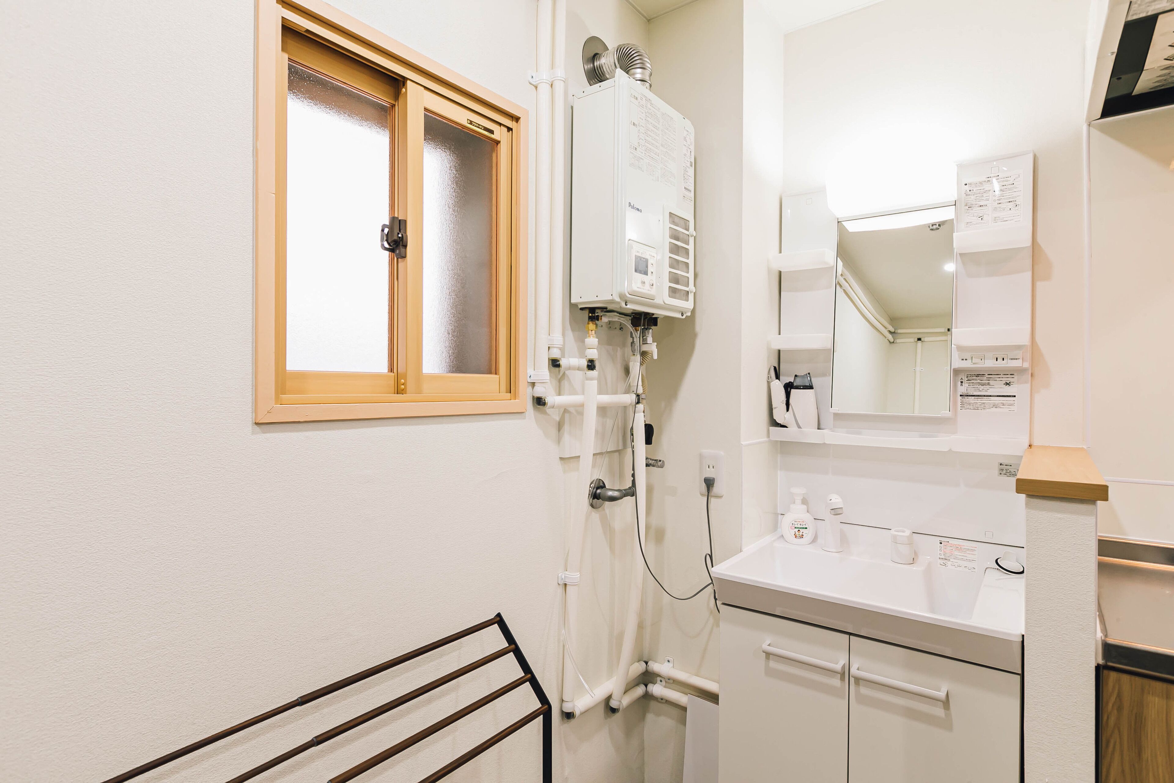 A bathroom with a white sink, a mirror, a towel rack, and a window with a wooden frame.