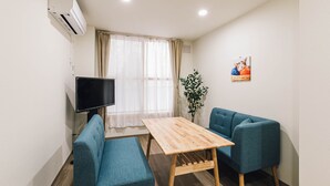 Une petite pièce avec une table en bois, deux canapés bleus, un téléviseur et une plante.