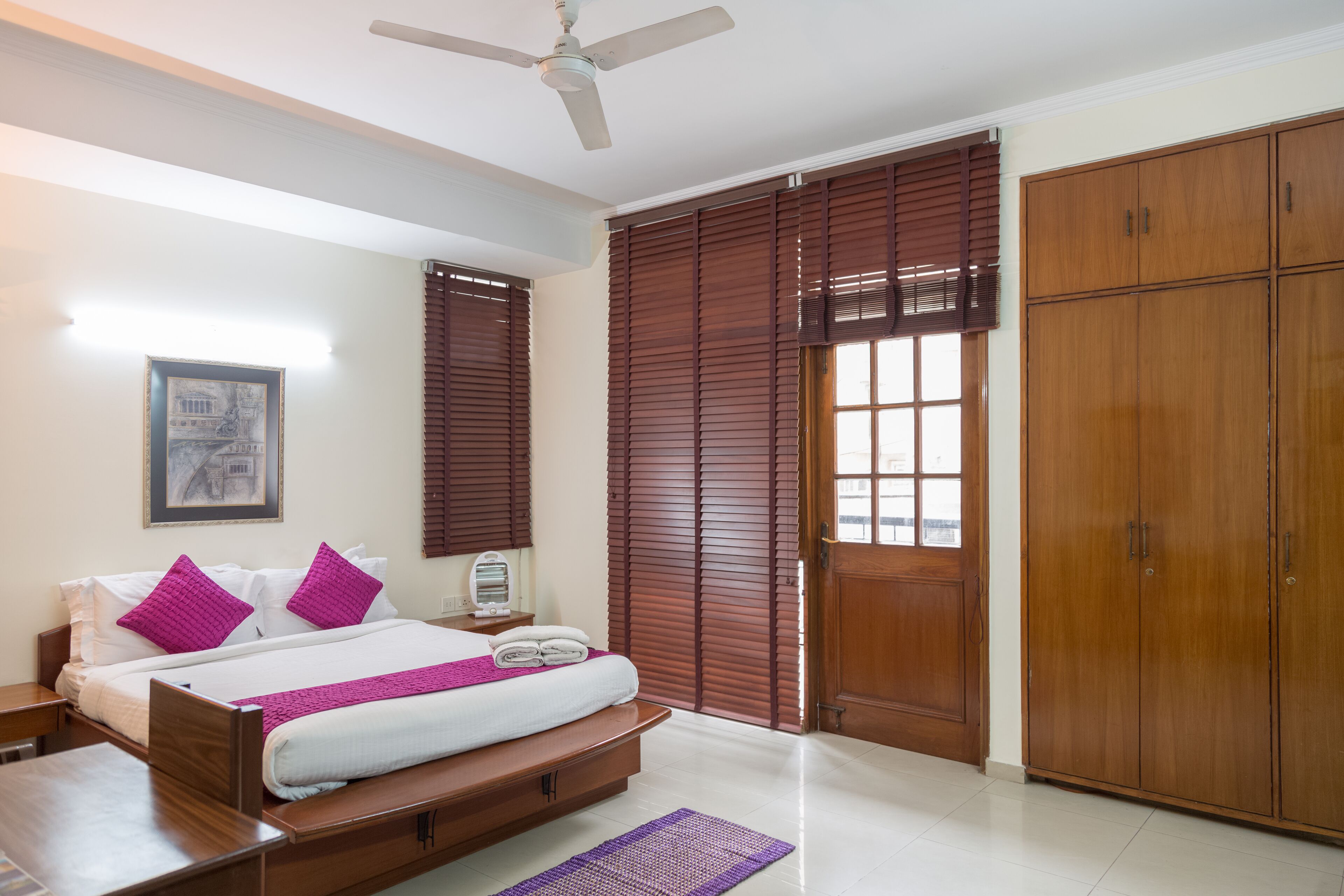 A bedroom with a bed, wooden wardrobe, and a ceiling fan.