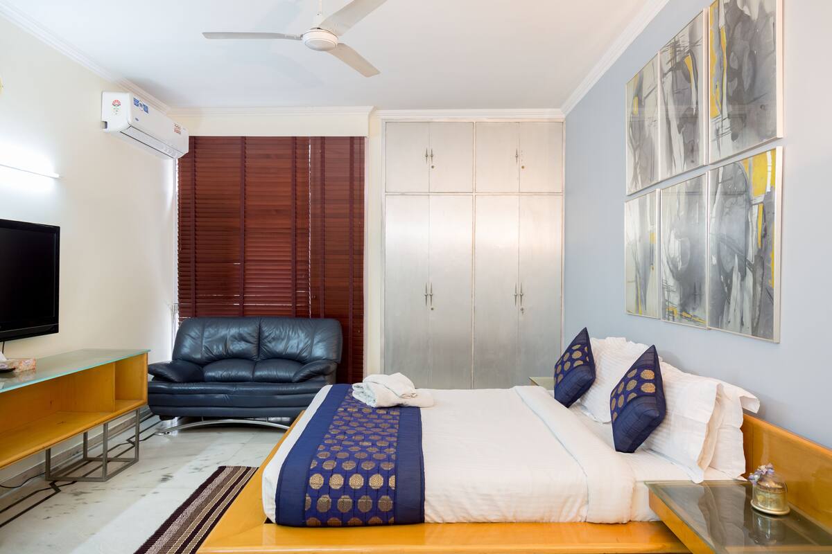 Habitació d'hotel amb un llit, un televisor, una butaca de cuir, un armari i obra d'art a la paret.
