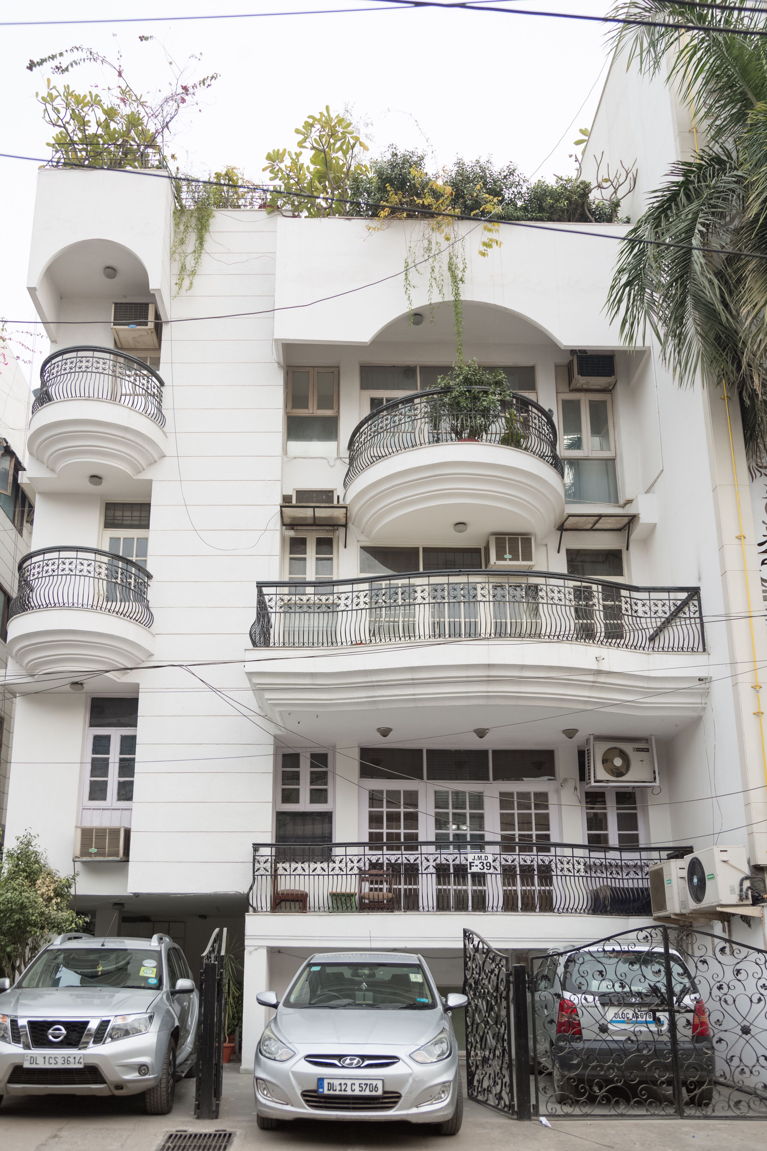 A multi-story building with balconies, a gated entrance, and parked cars.