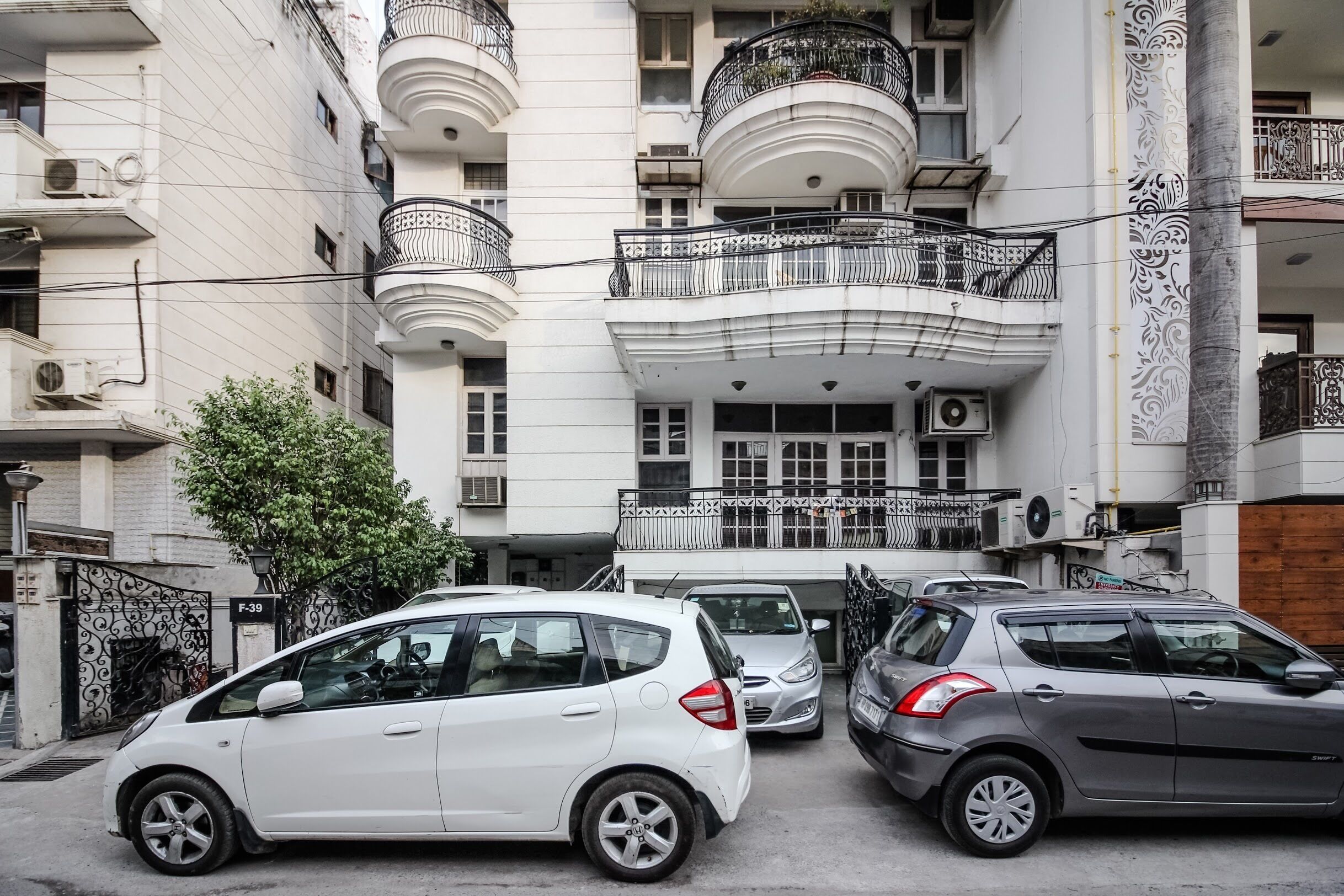 A multi-story building with balconies, parked cars, and a gate labeled "F-39".