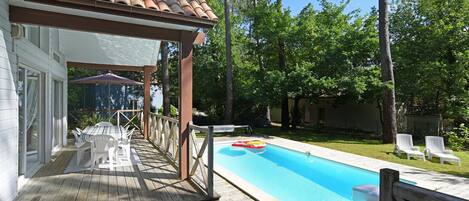 Une terrasse en bois avec une piscine, des chaises longues blanches et un espace patio couvert.