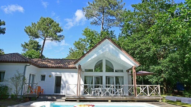 Una casa de dos pisos con piscina frente a ella, rodeada de árboles.