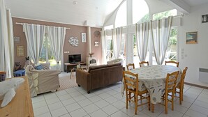 Amplia sala de estar con un gran ventanal, televisión y una mesa de comedor con sillas.