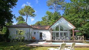 Una casa de dos pisos con piscina, un porche cubierto y un jardín con sillas de jardín.