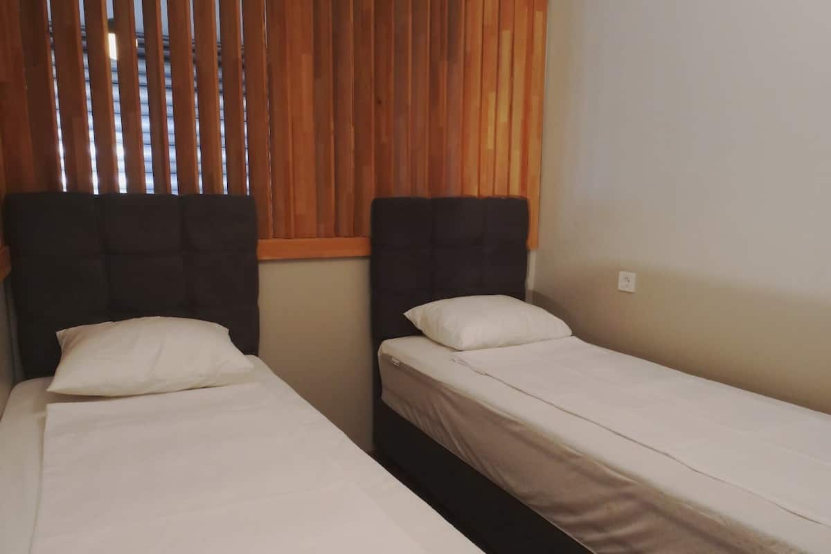 Two single beds with headboards, a window with vertical blinds, and a plain wall.
