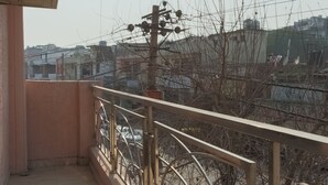 Un balcon doté d’une balustrade en métal, d’un sol carrelé et offrant une vue sur un paysage urbain avec des bâtiments et des arbres sans feuilles.