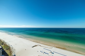 A beach with clear blue water, a sandy shore, and a few people. There are lounge chairs and umbrellas on the beach. - Panama Paradise Grand Panama 1803-Beachfront-Breathtaking Views-2Bd+Daybed/2Ba/Sleeps 8 (Panama City Beach)