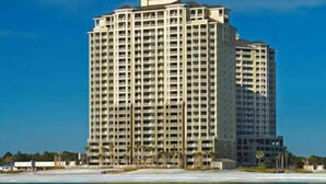 Un hotel moderno de gran altura con varios pisos, cerca de una playa bajo un cielo azul despejado.