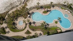Vista aérea de un resort con una gran piscina central, rodeado de palmeras y tumbonas.