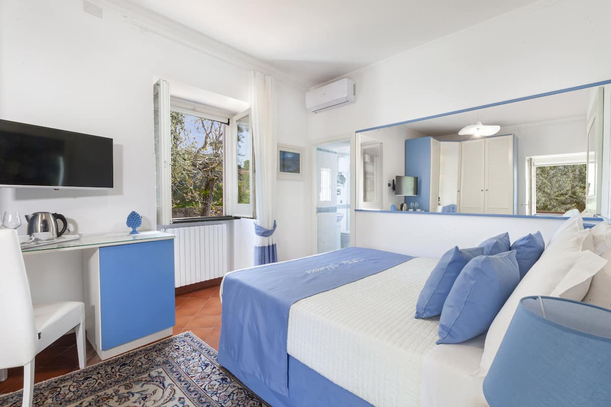 Une chambre à coucher avec un lit, un bureau, une chaise, un téléviseur et une fenêtre avec des rideaux.