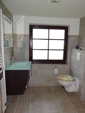 Ein Badezimmer mit großem Fenster, Waschbecken, Toilette und Spiegel.