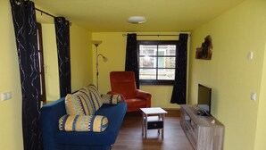 A living room with a blue sofa, an orange chair, a small table, and a wooden cabinet. - Urlaub mit dem Haustier im Wald (Rostock-Wiethagen)