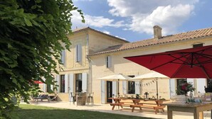 Une cour avec des sièges en plein air, un parasol rouge et un bâtiment doté d’un toit en tuiles.