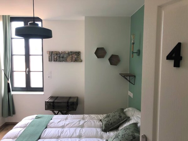 Une chambre avec un lit, une fenêtre, un numéro « 4 » fixé au mur et une étagère hexagonale.