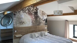 Une chambre à coucher avec un grand lit, un miroir rond, un radiateur fixé au mur et une fenêtre avec des rideaux.
